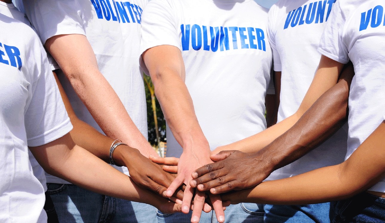 Associazione-Primo-Nebiolo Torino In primo piano: le mani di otto persone sovrapposte al centro, formano una sorta di “cerchio di cooperazione” Le mani con tonalità di pelle diverse, a sottolineare il valore della diversità, inclusività e integrazione. Tutti indossano magliette bianche con la scritta “VOLUNTEER” in blu ben visibile, che identifica chiaramente il gruppo di volontariato.